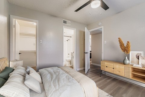 A bedroom with a bed, a ceiling fan, and a flat-screen TV mounted on the wall.
