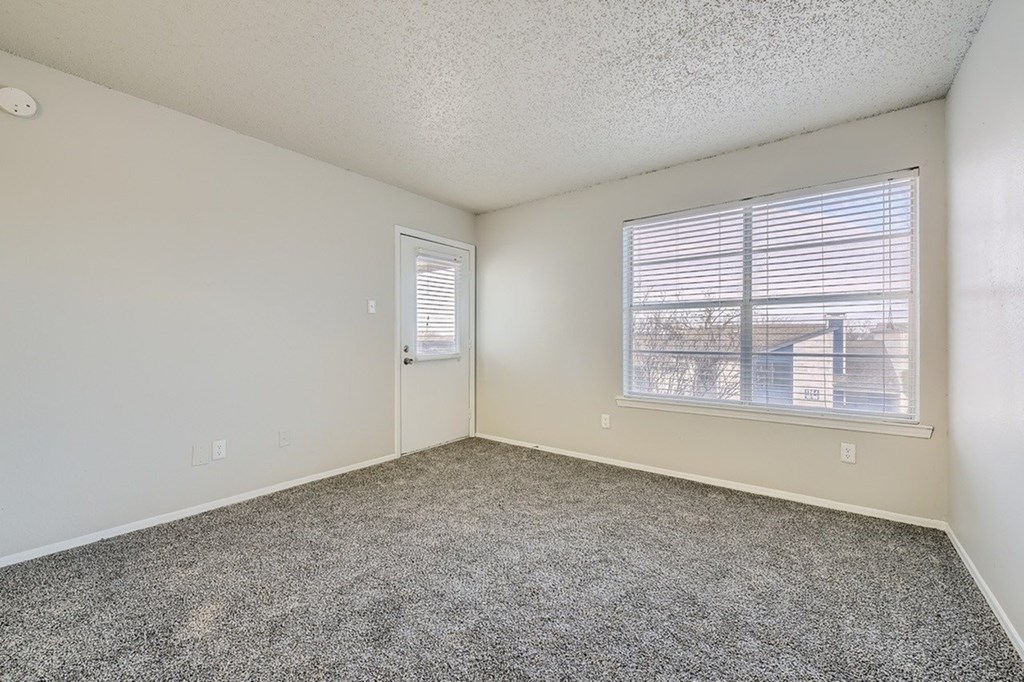 A room with a carpeted floor and a window with blinds.