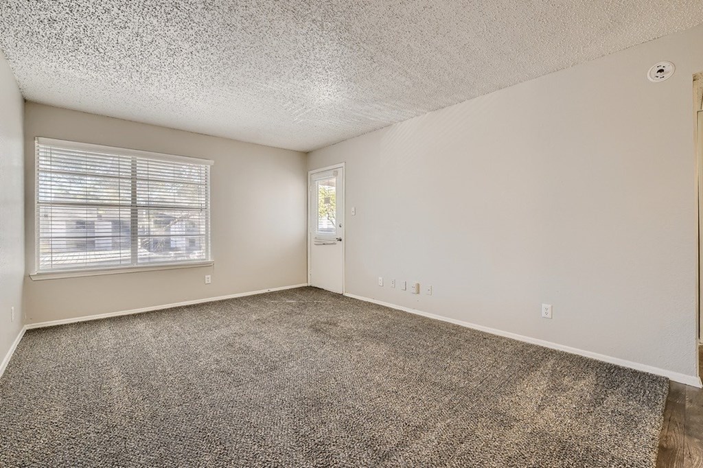 A room with a carpeted floor and a window with blinds.