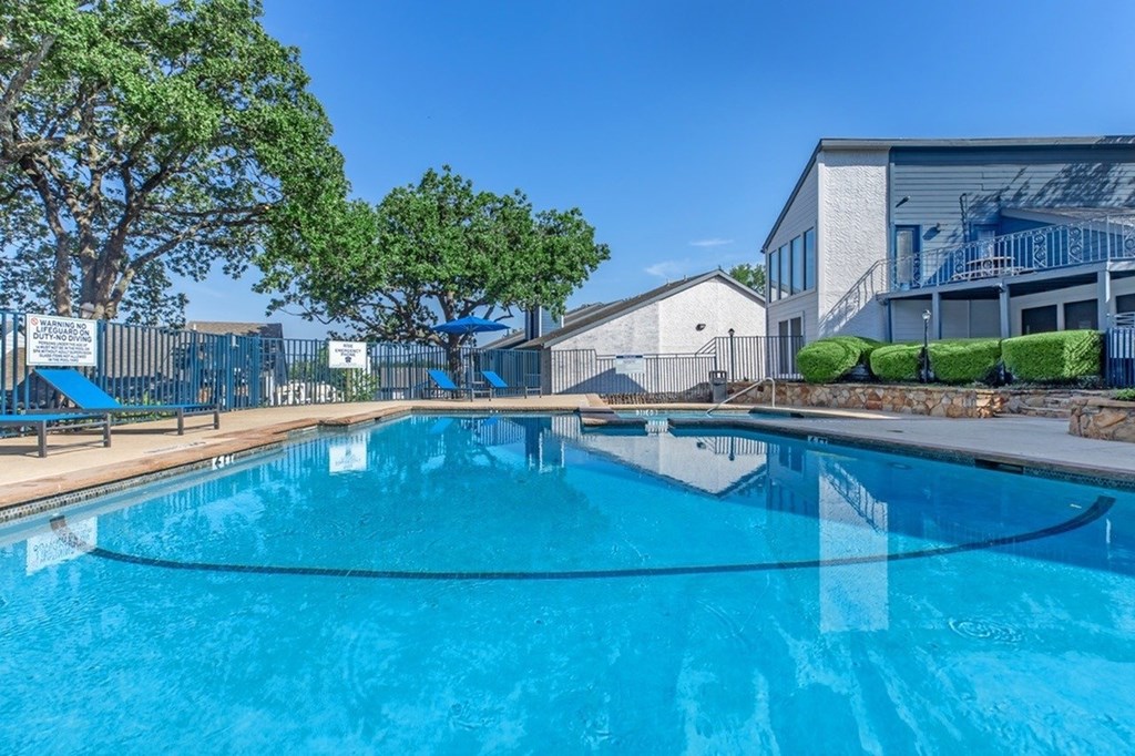A large blue swimming pool with trees and a building in the background.