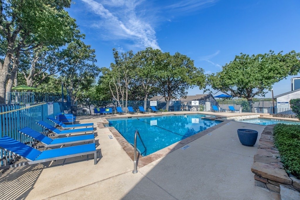 A pool surrounded by trees and blue lounge chairs.