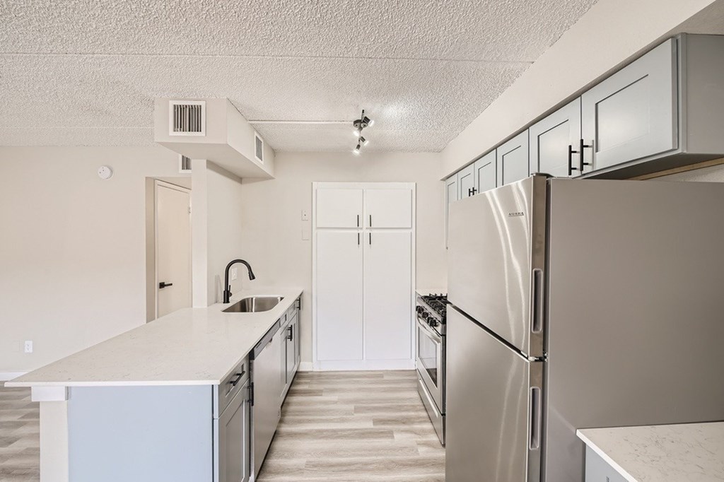A kitchen with a refrigerator, sink, and cabinets.