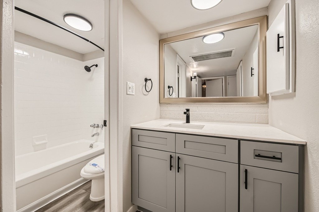 A bathroom with a white tub and grey cabinets.