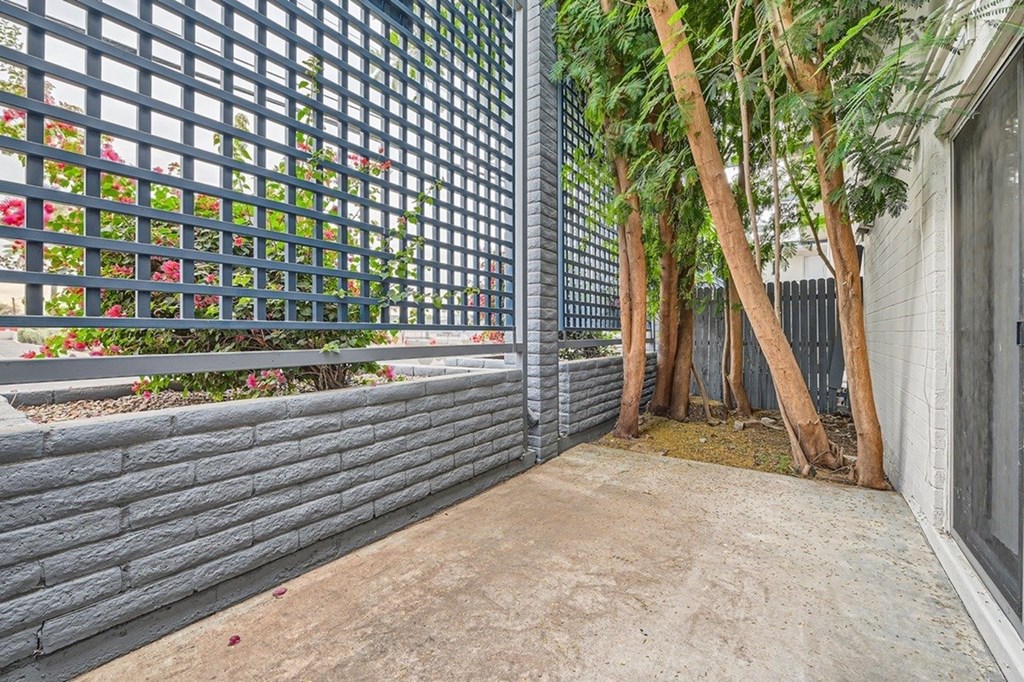 A metal fence with a lattice pattern separates a garden area from a concrete pathway.
