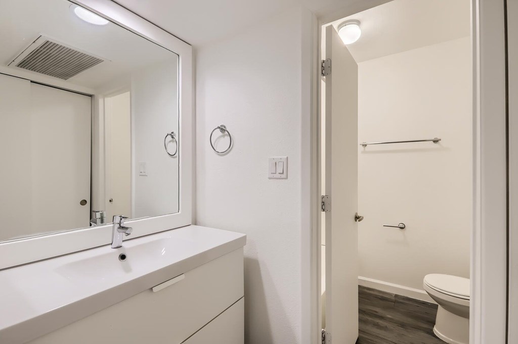 A white bathroom with a sink, mirror, and toilet.