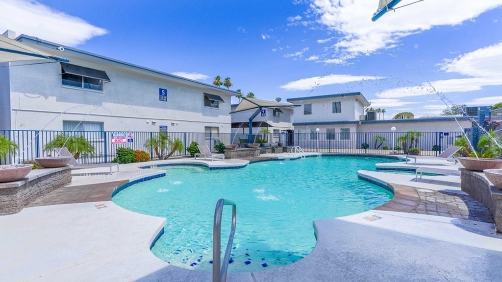 A swimming pool surrounded by a concrete patio and a metal fence.