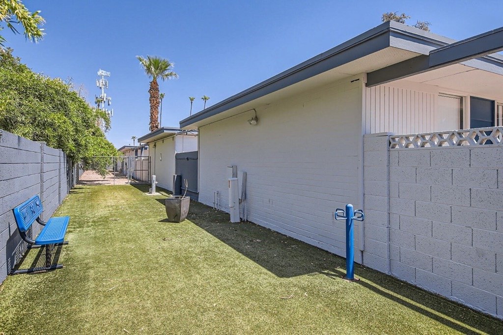 A blue bench sits in a yard next to a white house.