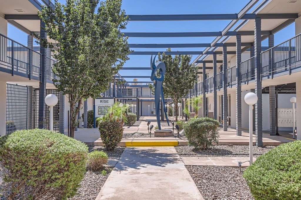 A sculpture of a person holding a globe is in the center of a courtyard with trees and bushes.
