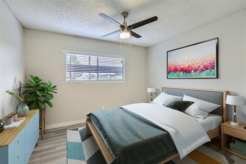 A bedroom with a bed, a ceiling fan, and a painting on the wall.
