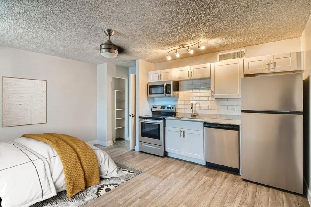 A modern kitchen with stainless steel appliances and a bedroom with a yellow throw.