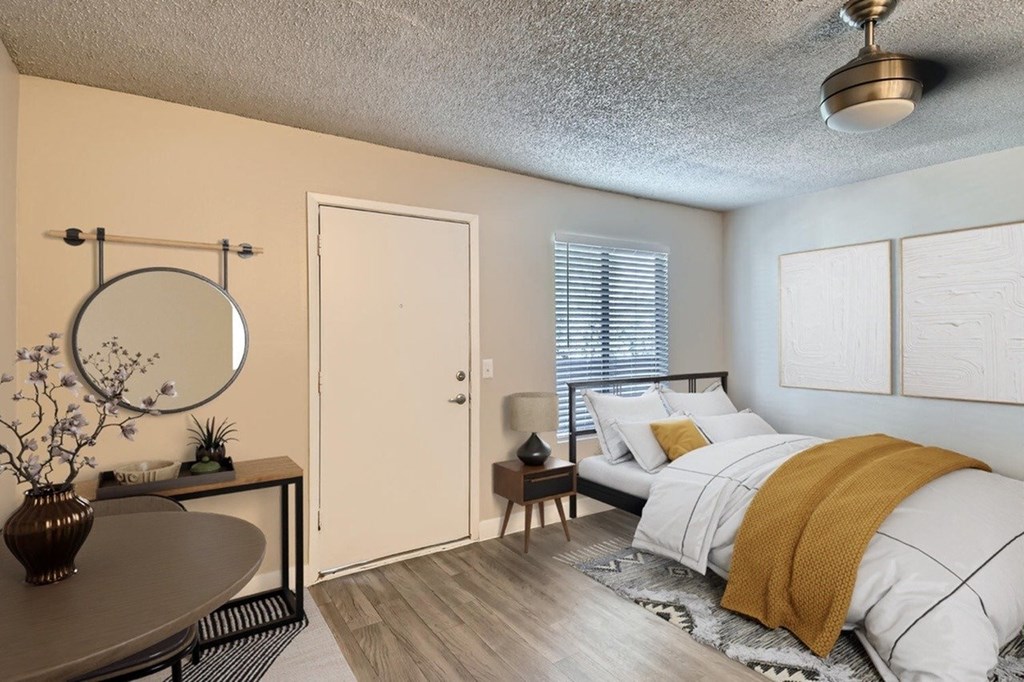 A bedroom with a bed, a round table, a mirror, and a vase on the table.