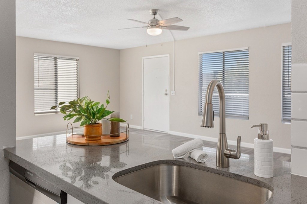 A kitchen with a grey counter top and a stainless steel sink.
