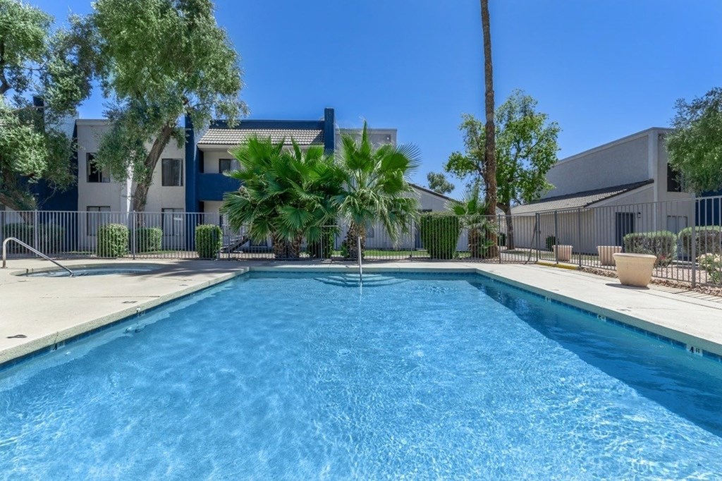 A swimming pool in front of a building with a fence and trees.
