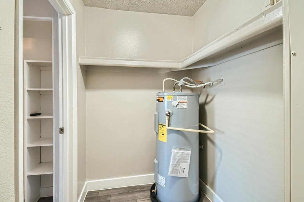 A small room with a white wall and a grey water heater.