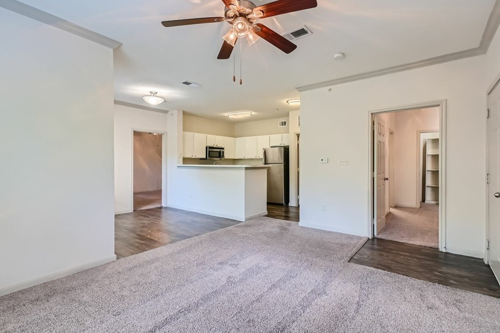 A spacious living room with a ceiling fan and a kitchen in the background.