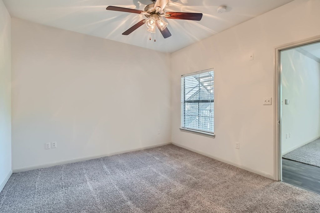 A room with a ceiling fan and a window with blinds.