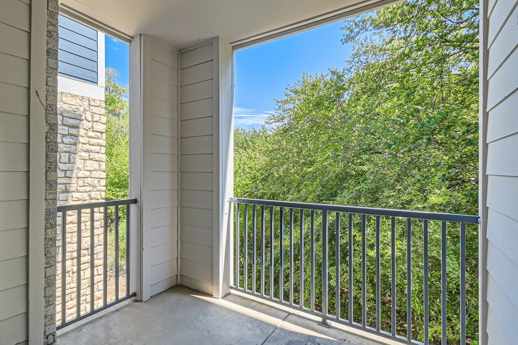 A balcony with a metal railing and a view of a green tree.