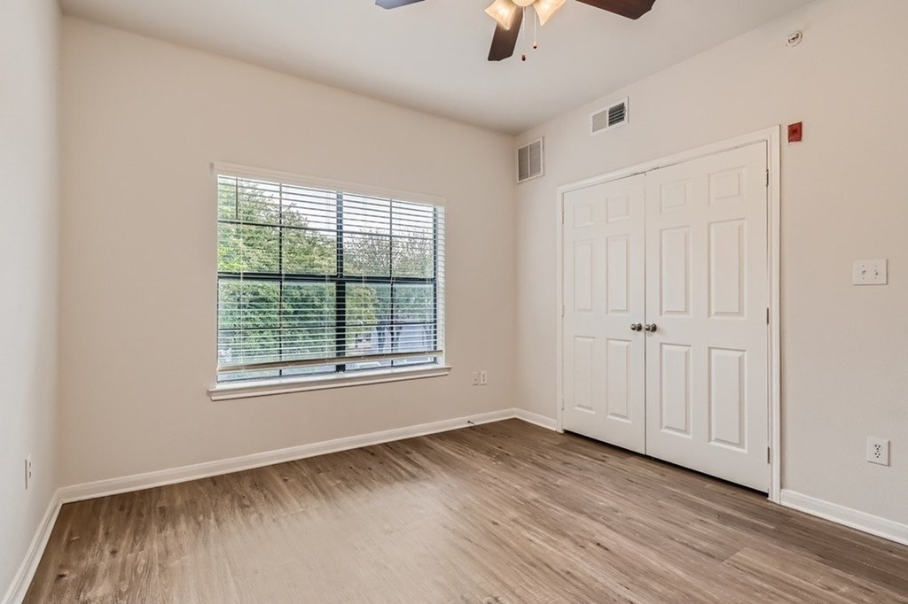 A room with a white door, a window with blinds, and a ceiling fan.