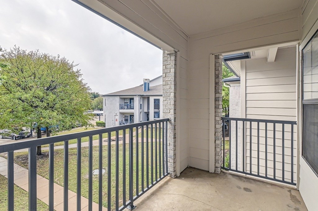 A balcony with a black railing and a view of a building and trees.