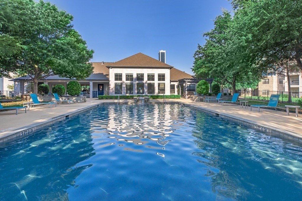 A swimming pool in front of a building with trees on the sides.