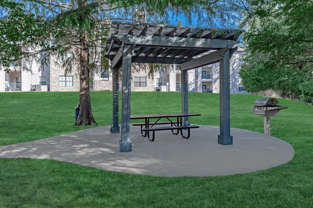 A picnic area with a bench and a canopy is set in a grassy area.