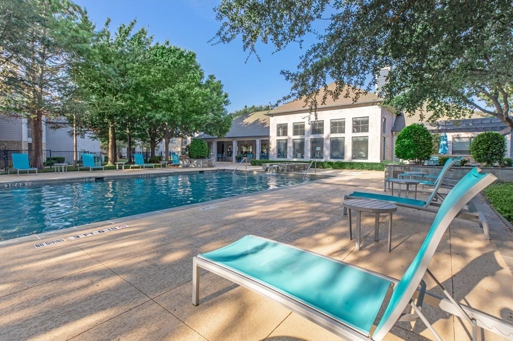 A pool with a sun lounger in front of a white building.