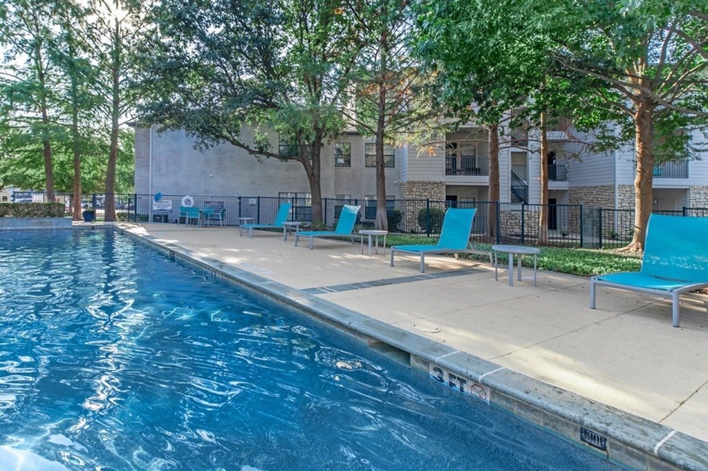 A swimming pool with blue water and a concrete edge with a bench on it.