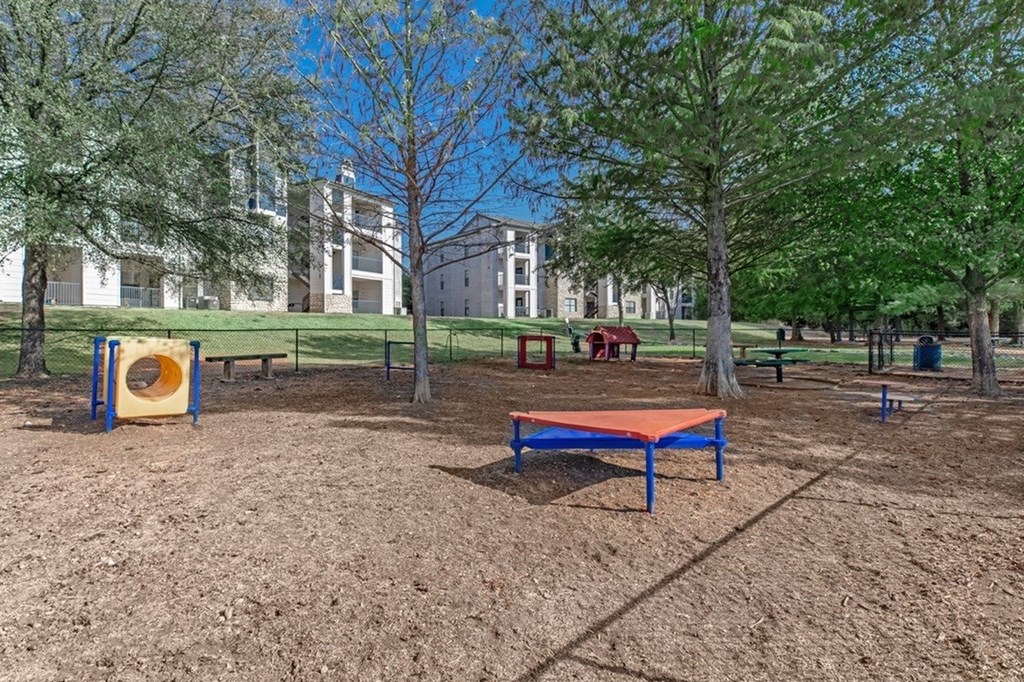 A playground with a slide, swing set, and trampoline in a park.