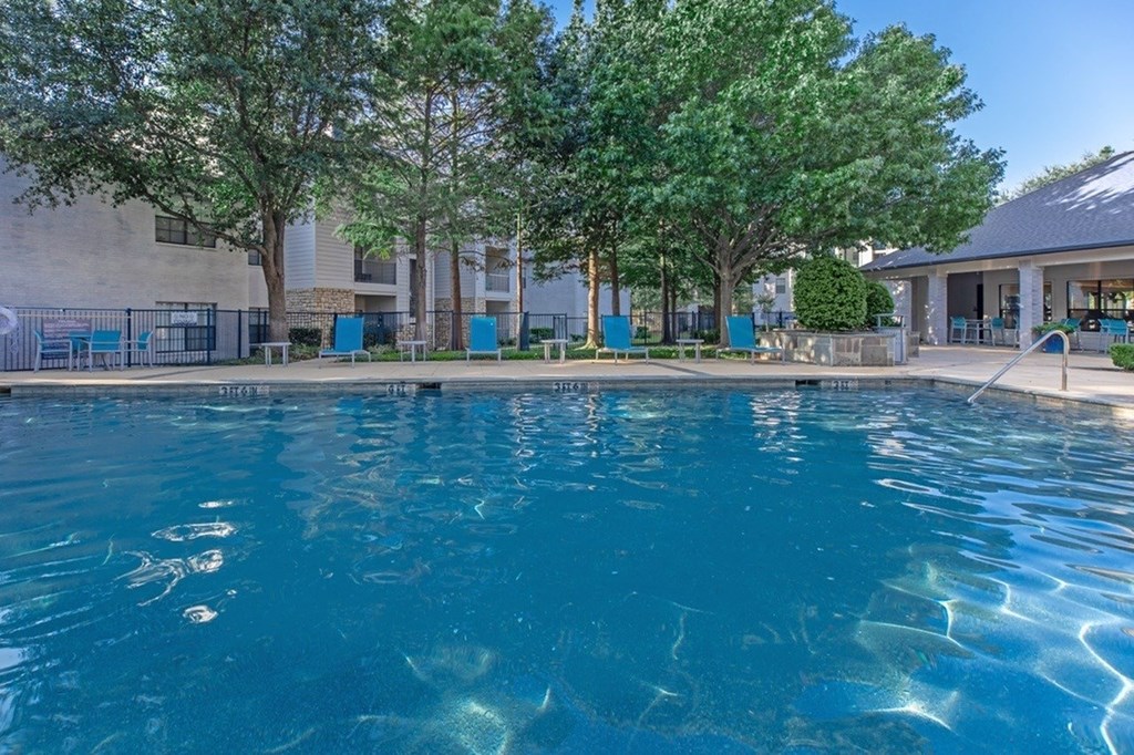 A swimming pool surrounded by trees and a building in the background.