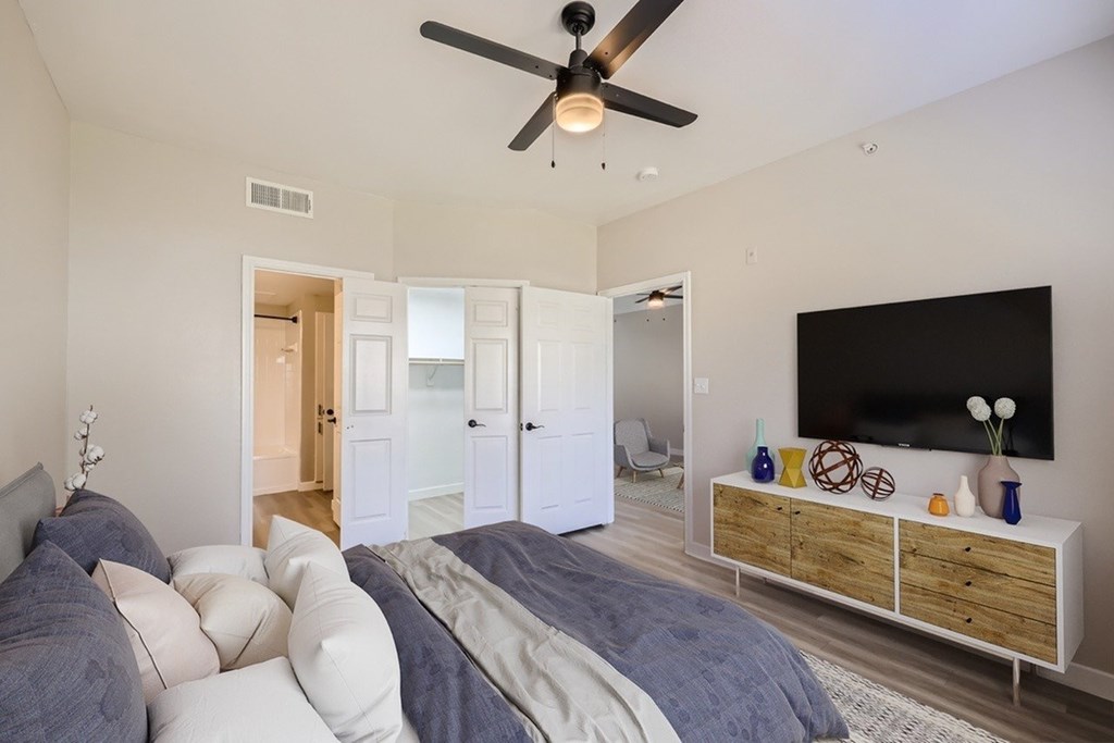 A bedroom with a bed, a ceiling fan, and a TV on a cabinet.