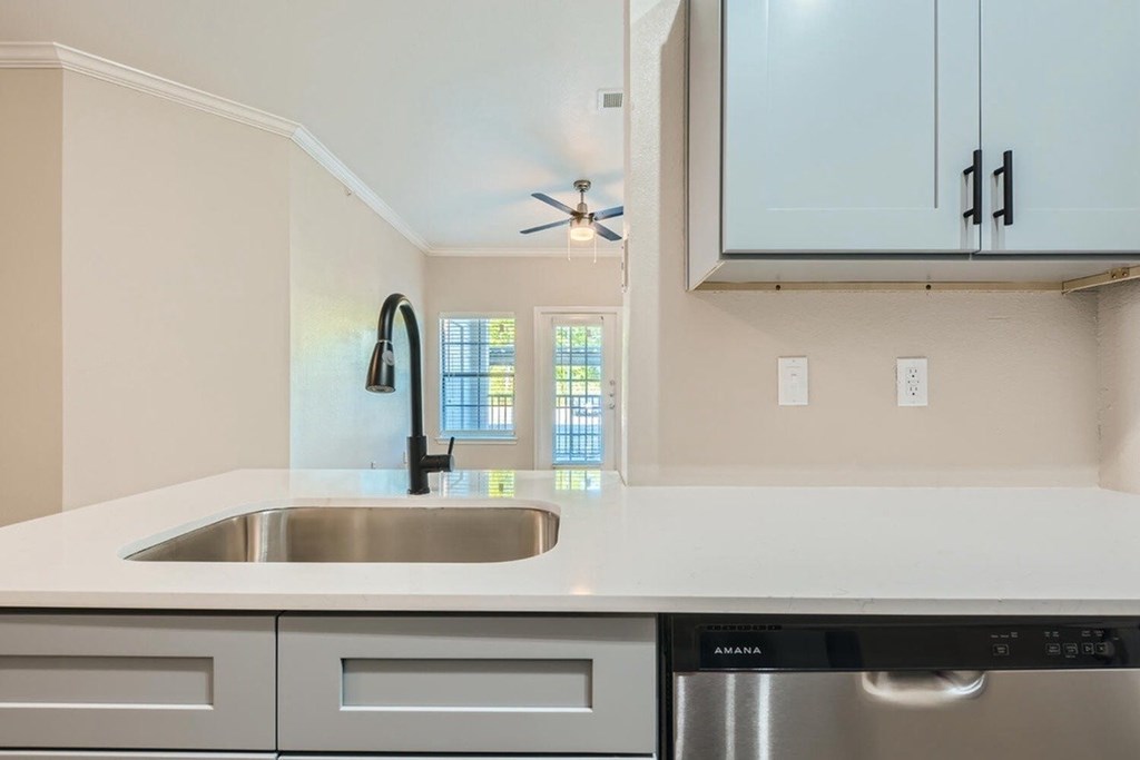 A modern kitchen with a stainless steel dishwasher and a window above the sink.