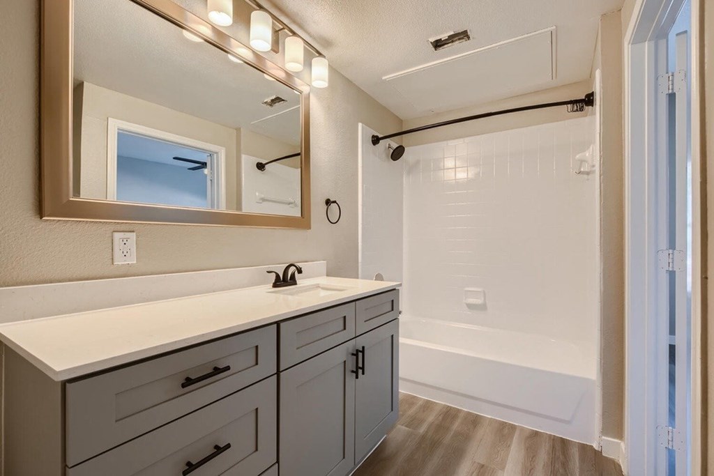 A bathroom with a vanity, mirror, and a bathtub.