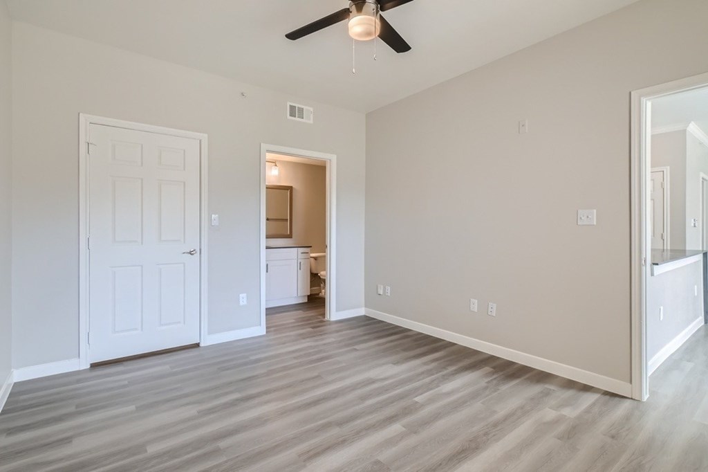 A room with a ceiling fan and light, hardwood floors, and white walls.