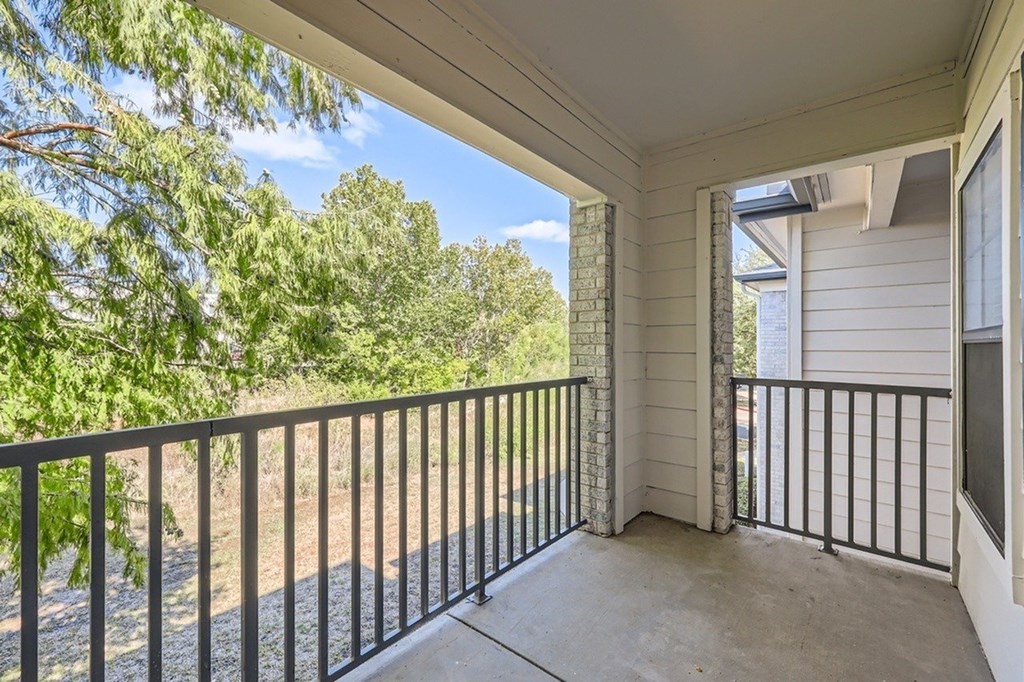 A balcony with a black railing and a view of trees and a clear sky.
