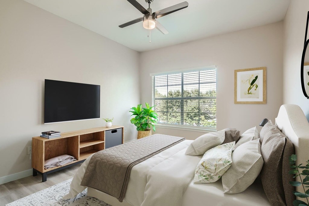 A bedroom with a bed, a television, and a window with blinds.