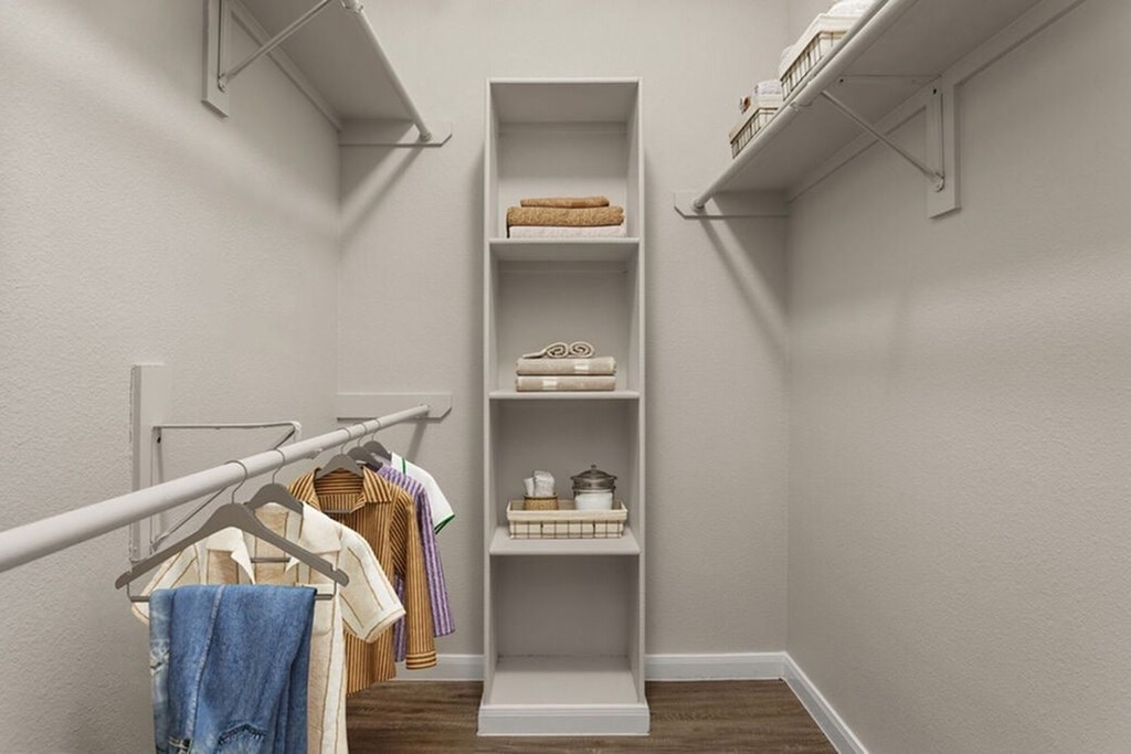 A white closet with clothes hanging and shelves with towels and other items.