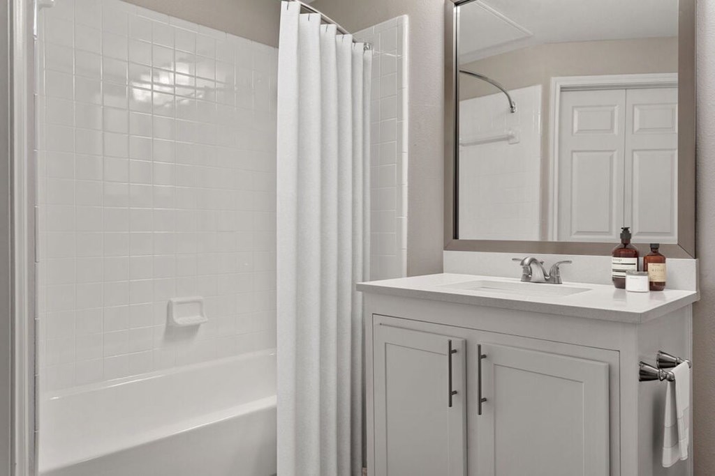A white bathroom with a white tub, sink, and shower curtain.