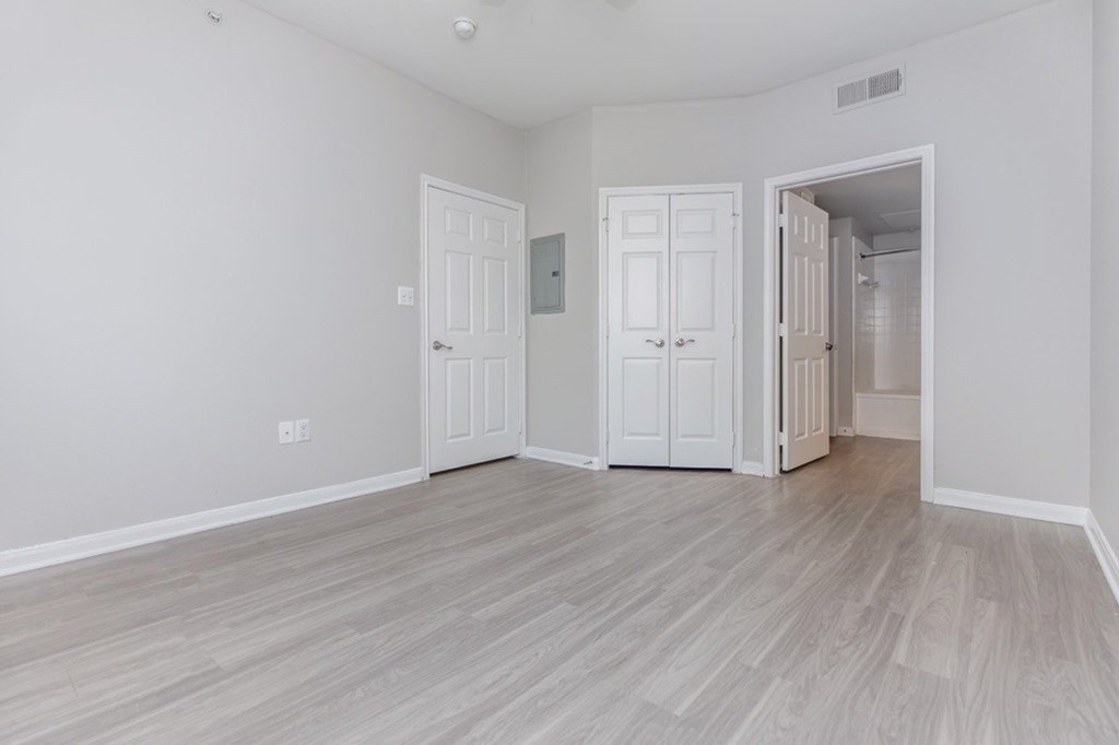 A room with white walls and wood flooring with two doors.