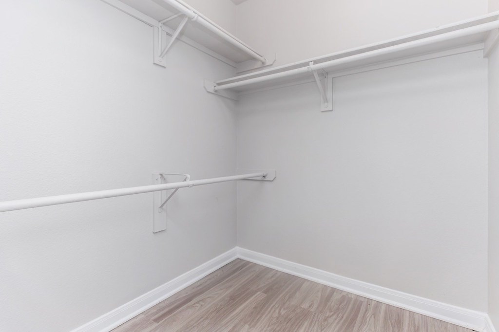 A white wall with a shelf and a wooden floor.