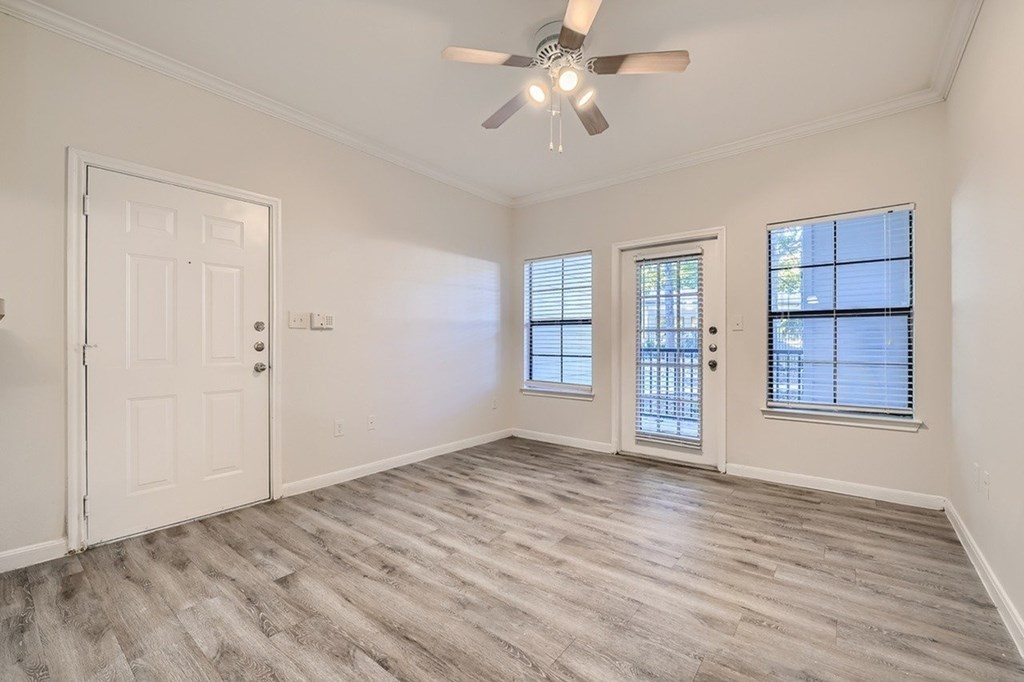 A room with a ceiling fan and light, hardwood floors, and two doors.
