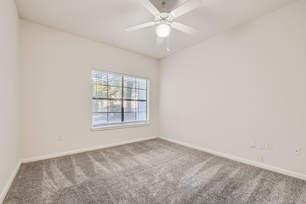 A room with a ceiling fan and a window with blinds.