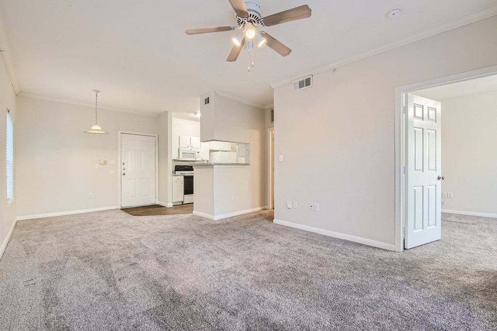 A spacious living room with a ceiling fan and carpeted floor.