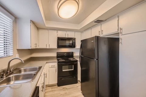 A black refrigerator sits in a kitchen with a stove and oven.