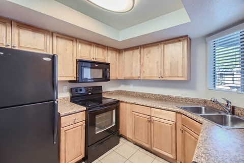 A kitchen with a black refrigerator, black stove, and black microwave.