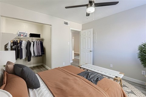 A bedroom with a bed, pillows, a ceiling fan, and a closet with clothes.