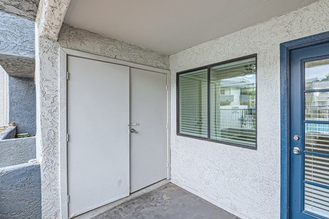 A white door is closed and a window with blinds is on the right.