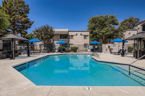 A swimming pool with a blue umbrella and a white building in the background.