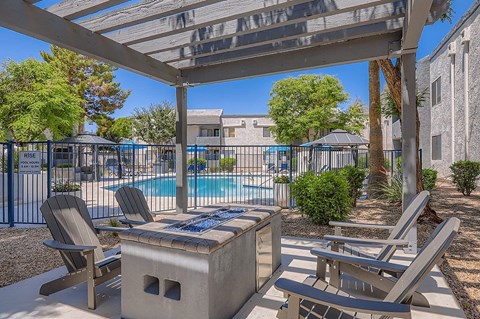 A sunny day at the pool with chairs and a table under a pergola.