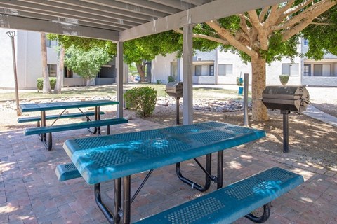 Picnic tables and benches under a canopy in a sunny outdoor area.
