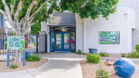 The image shows a building entrance with a blue door and a signboard on the left.